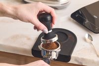 A person about the compact espresso grounds with the Pullman tamper.