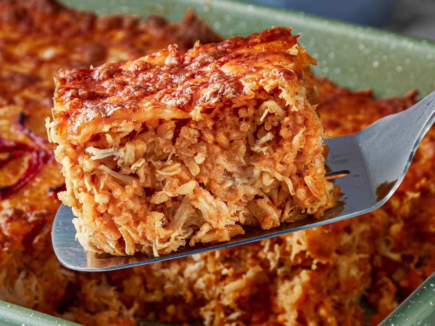 Closeup of a slice being served from a baked layered dish resembling Arroz Imperial