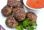 Close-up of grilled meatballs plated with a side of marinara