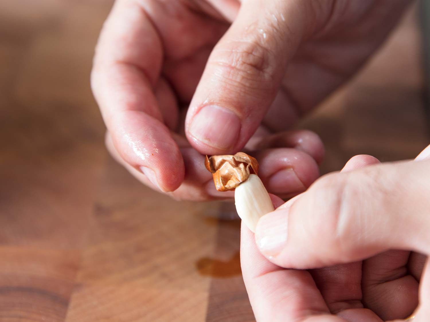 Two hands removing papery skin from a just-blanched almond.