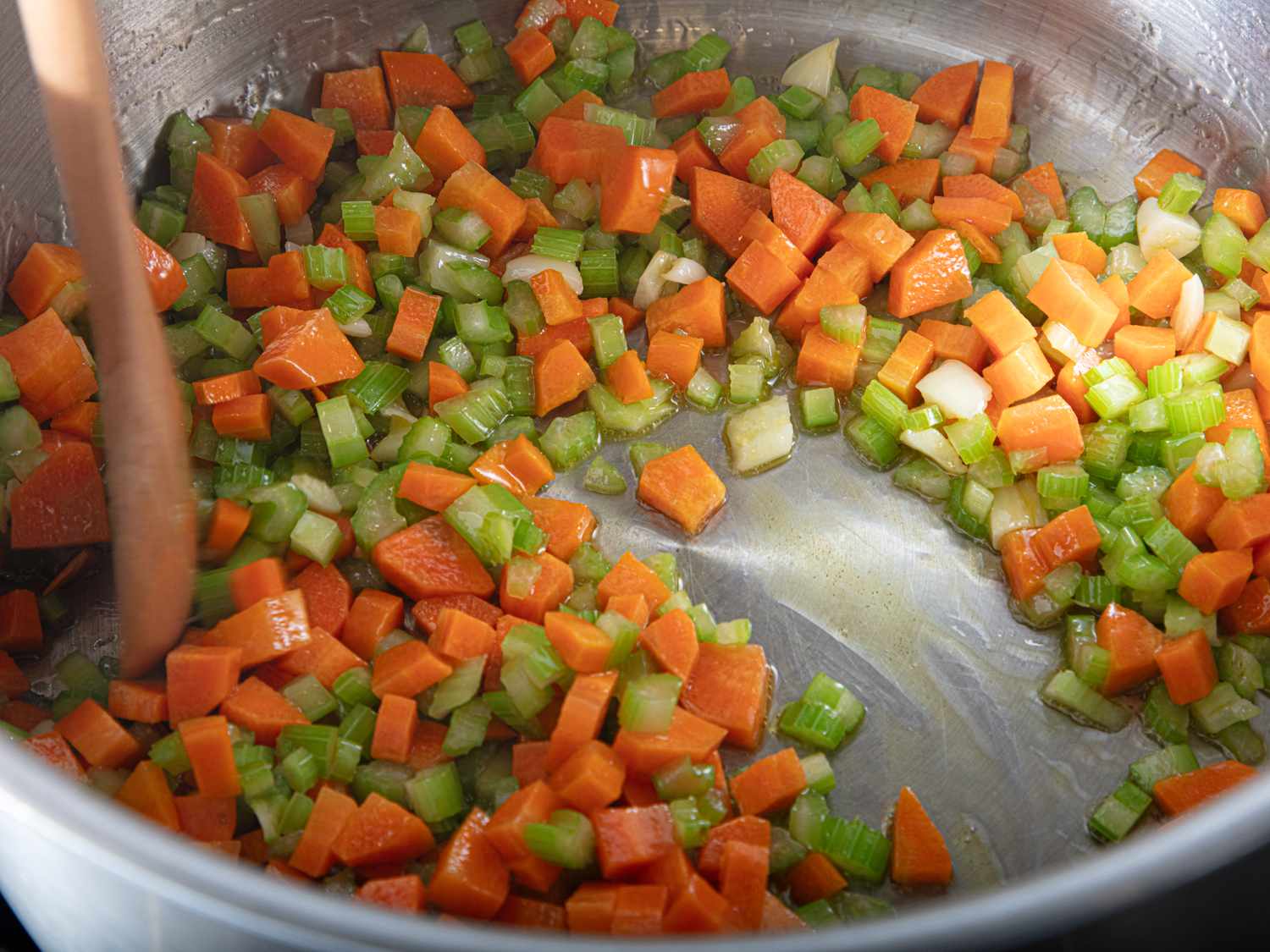 Diced carrots celery and onion being sauted in a pot with a wooden spoon