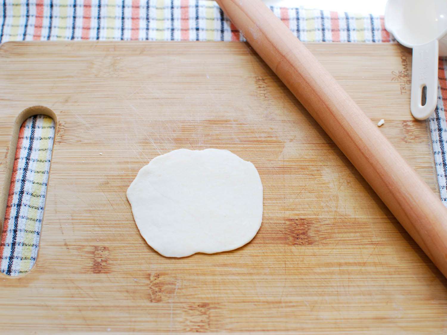 A rolled out wrapper for sheng jian bao on a cutting board.
