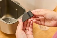 Two hands lifting a small part of the Zojirushi Home Bakery Mini Breadmaker