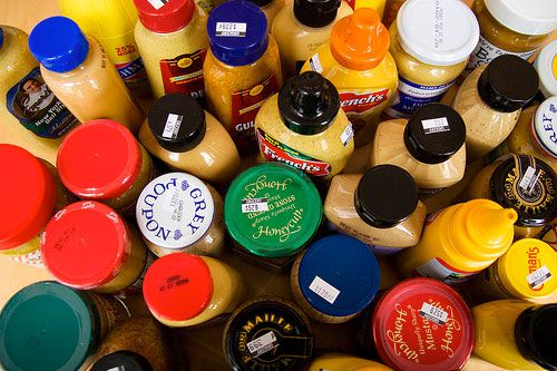 A tabletop full of different bottles and jars of mustards. 