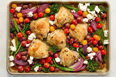 Sheet pan with roasted chicken thighs tomatoes red onions olives broccolini and feta cheese crumbles