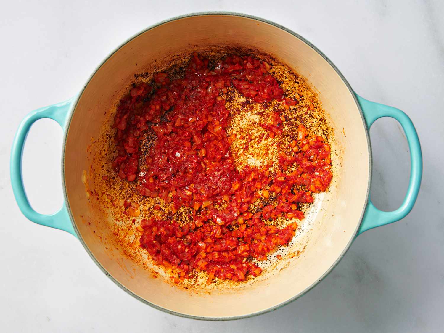 Softened onion and garlic and tomato paste in a Dutch oven, having cooked enough that the tomato paste has darkened.