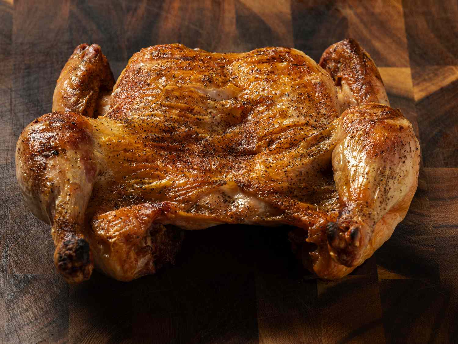 An angled shot of a golden brown crispy-skinned grilled chicken, breast-side up, on a wooden cutting board.