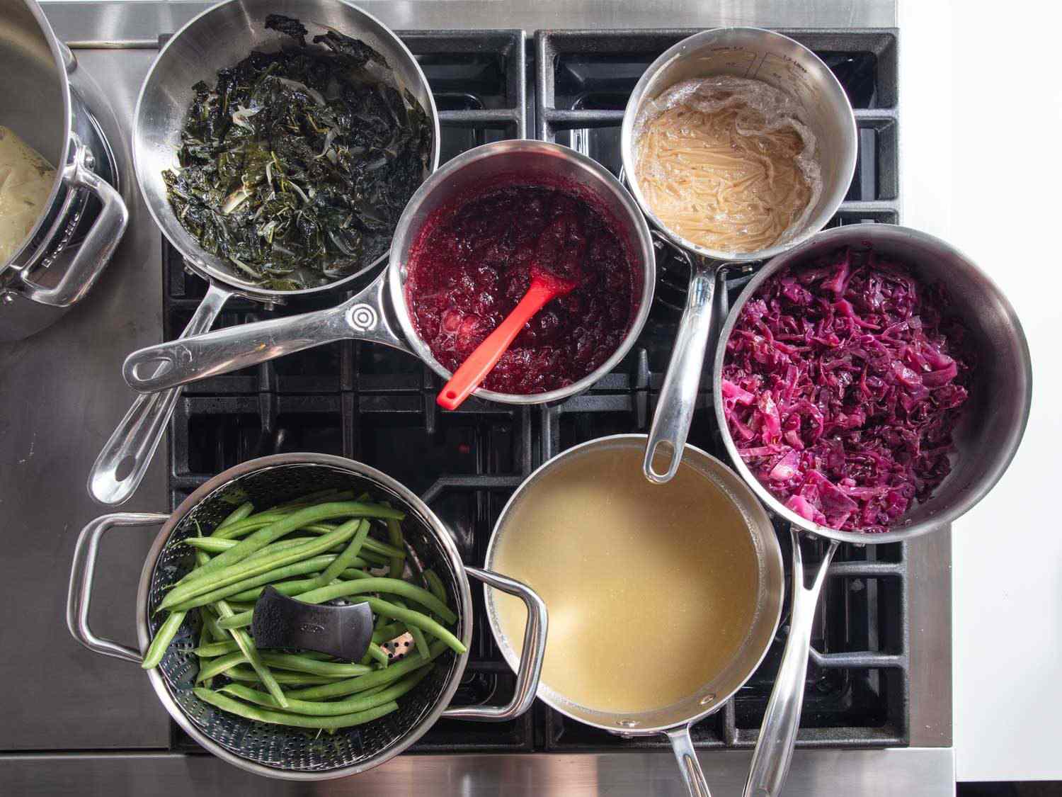 Overhead of saucepans jammed up on a gas range, with many of the saucepans not directly over burners.