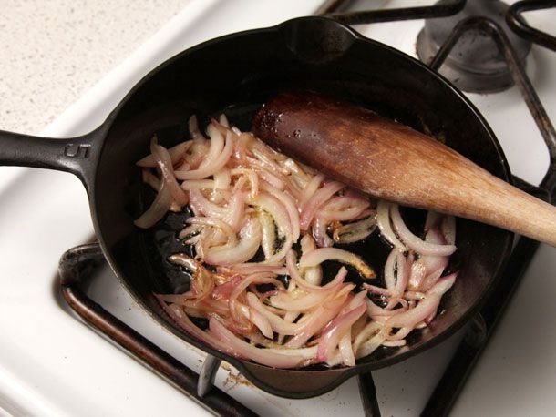 Sliced red onion is fried in a cast iron skillet.