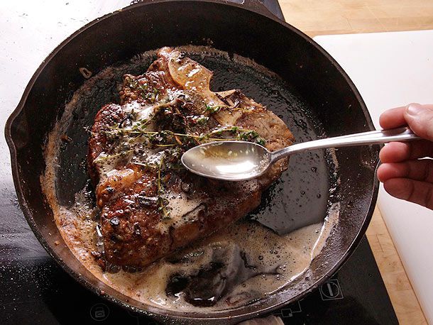 Butter and herb basting a T-bone steak in a hot cast iron skillet.