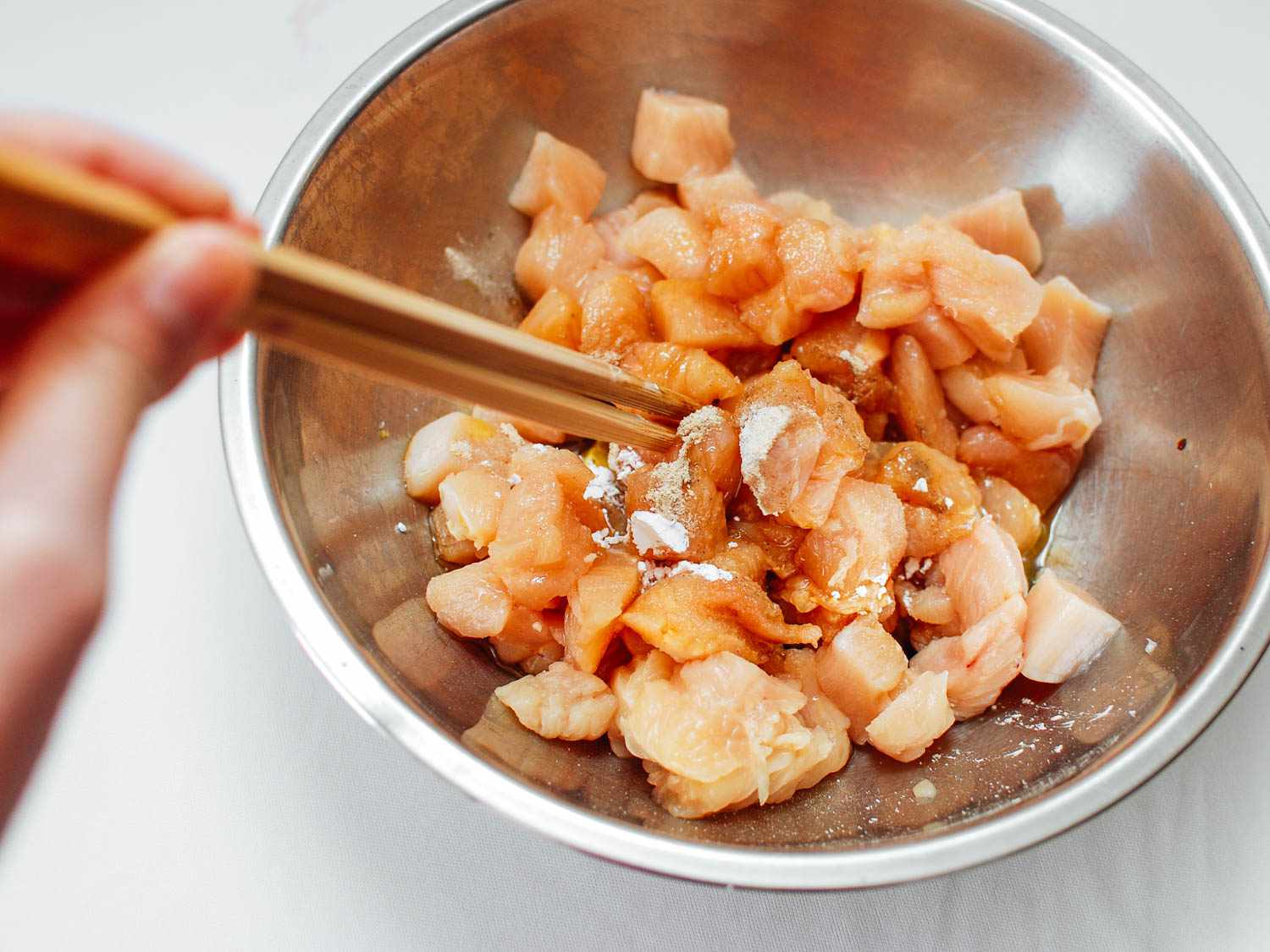 Using chopsticks to combine cubed chicken and marinade ingredients in a stainless bowl.