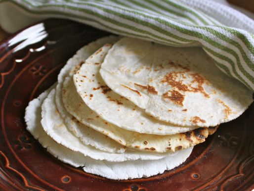Finished gluten-free tortillas on a plate. A dish towel is nearby to cover the tortillas and keep them warm.