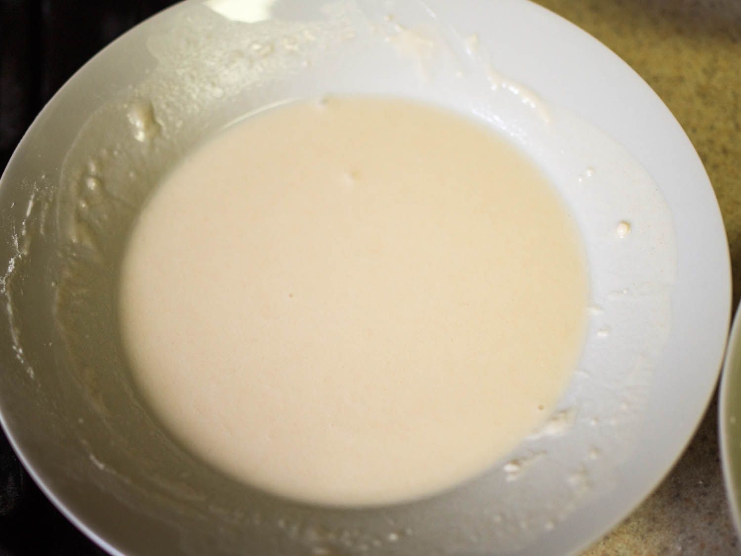 A white bowl filled with a slurry for dipping and frying arancini.