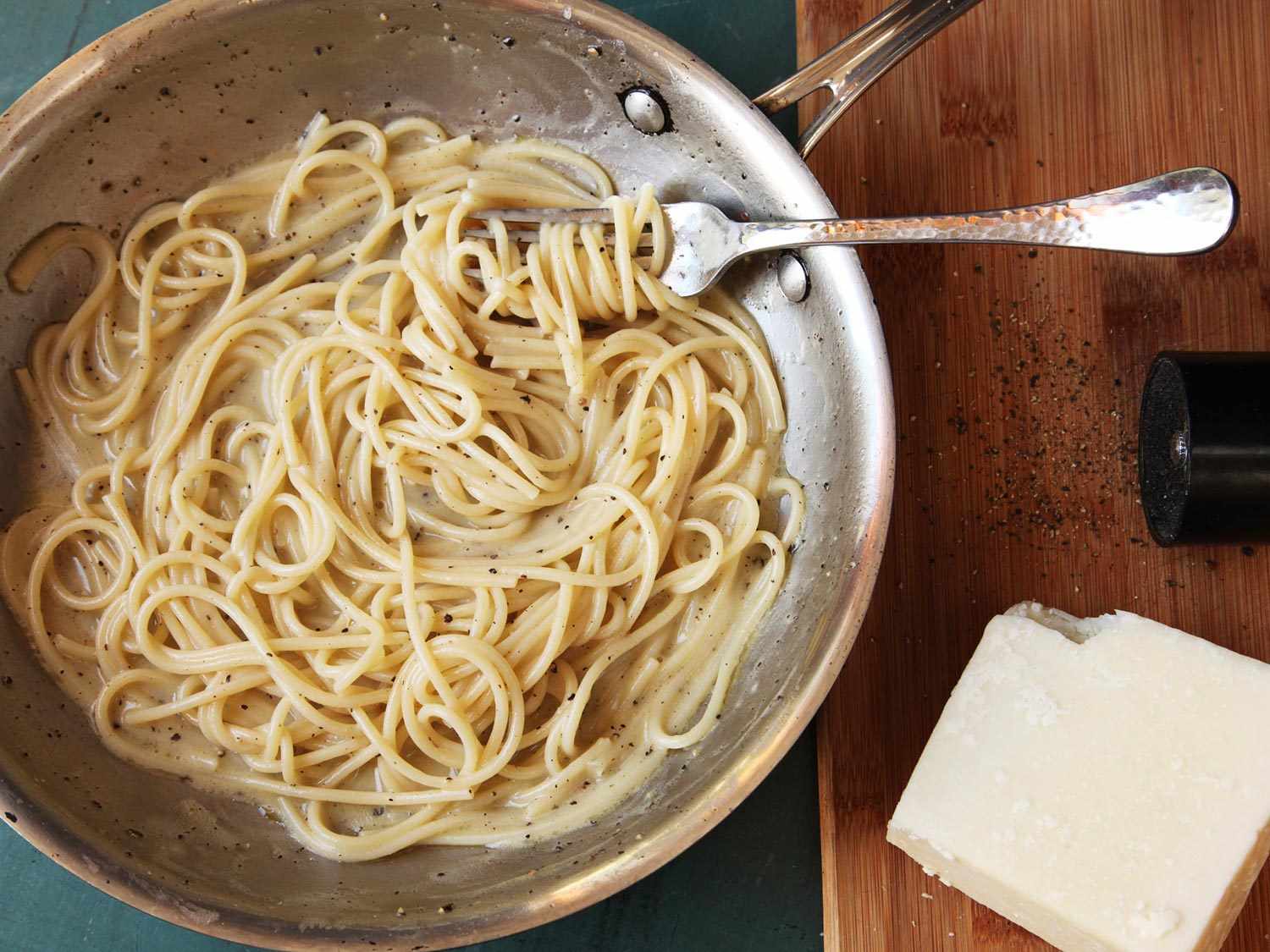 Overhead shot of a skillet of cacio e pepe pasta, next to a block of cheese and a pepper grinder.