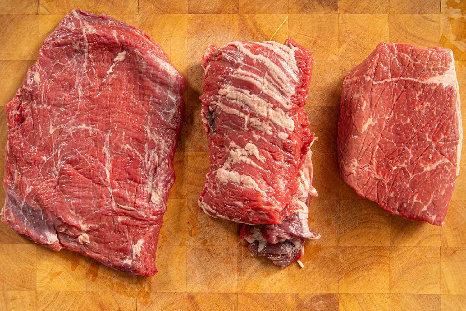 Three types of raw beef on a wooden cutting board.