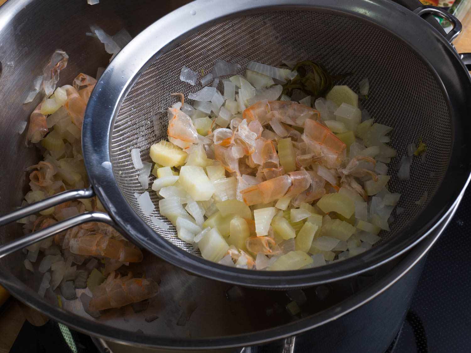Shrimp shells and other solids from broth being removed from pot with a small strainer.