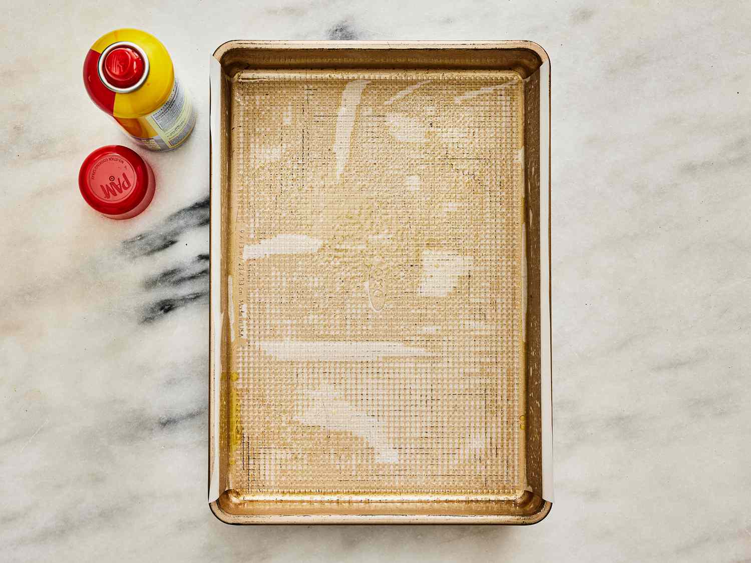A cooking pan with parchment paper, sprayed with cooking sprat. The bottle of spray is next to the pan with the lid off. 