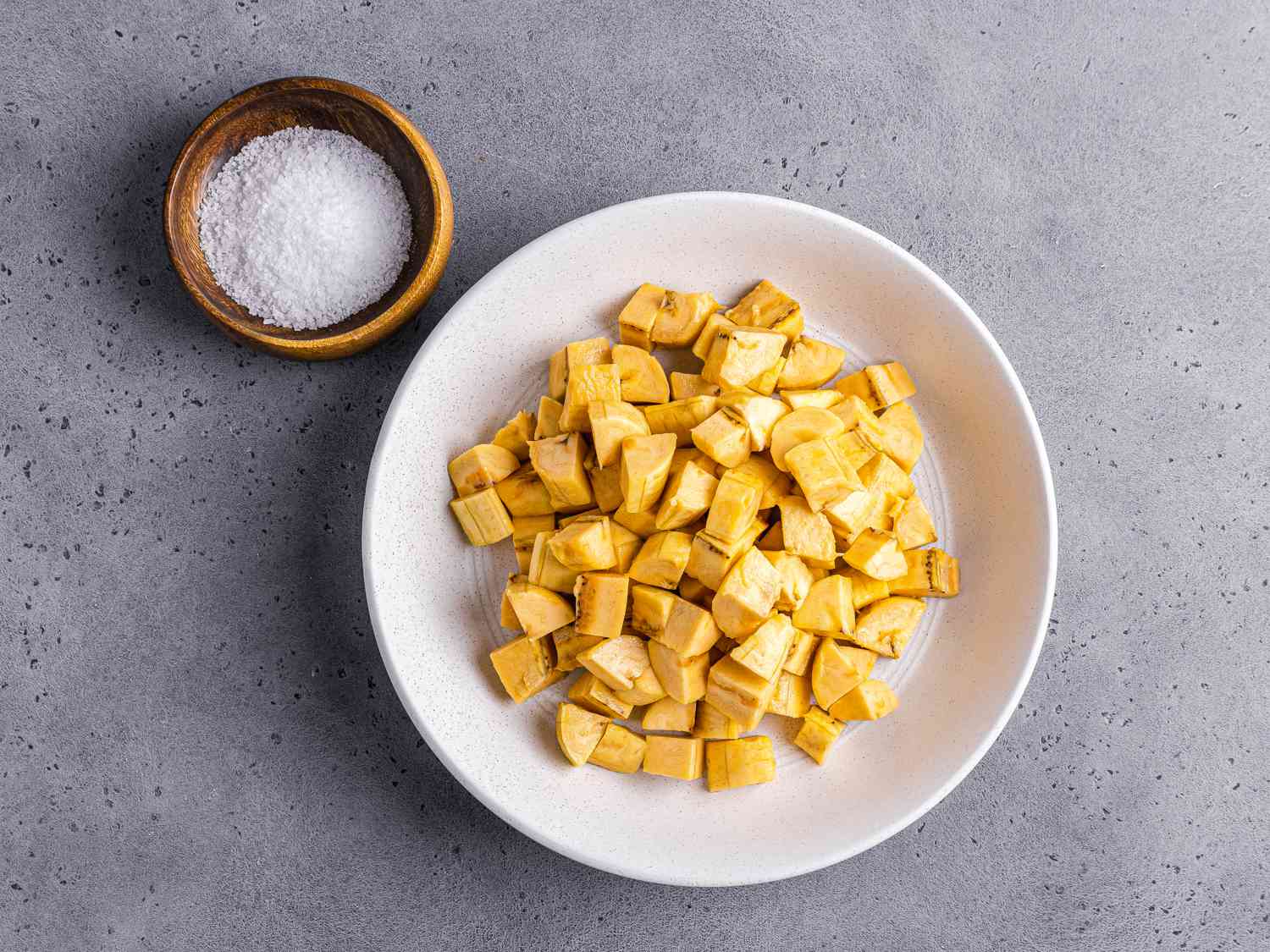 Diced plantains in a white bowl next to a small bowl of salt