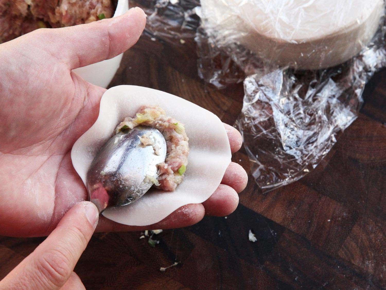 Dumplings being filled with meat mixture with a spoon.