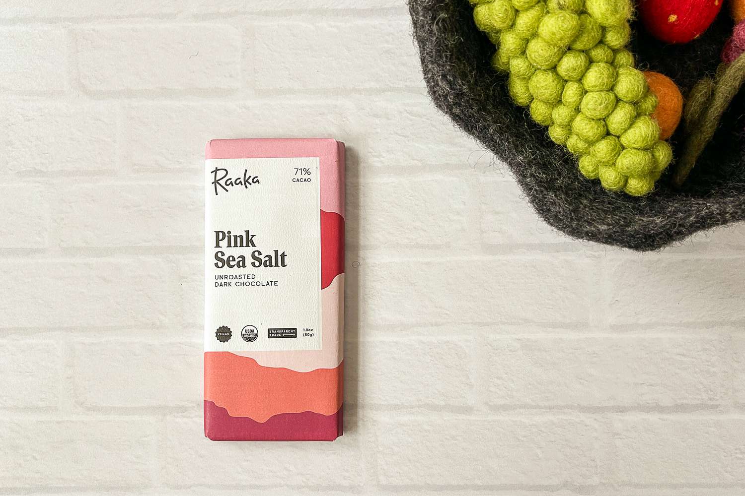 The Raaka Pink Sea Salt Dark Chocolate Bar on a white brick surface