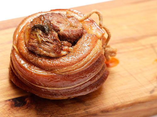 A fully braised log of chashu pork, standing on one end on a cutting board.