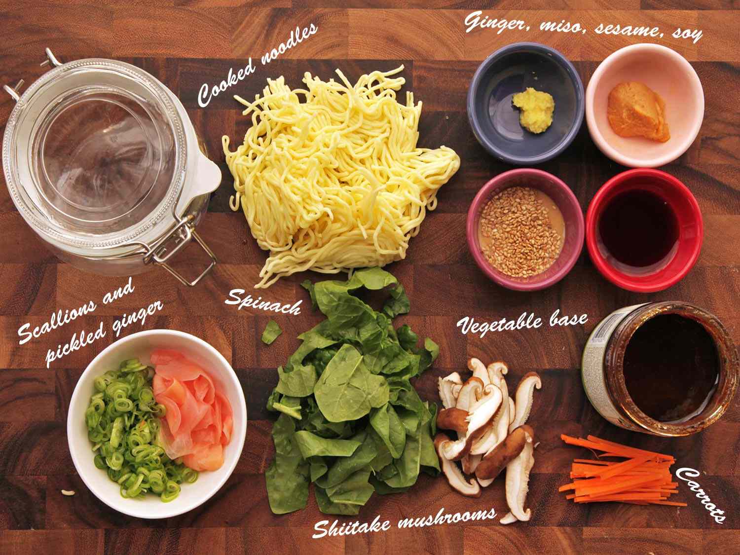 Overhead view of ingredients needed to make vegetable with sesame-miso soup flavor instant noodles: ginger, miso, sesame paste, soy, vegetable base, carrots, shiitakes, spinach, scallions, pickled ginger, and cooked noodles.