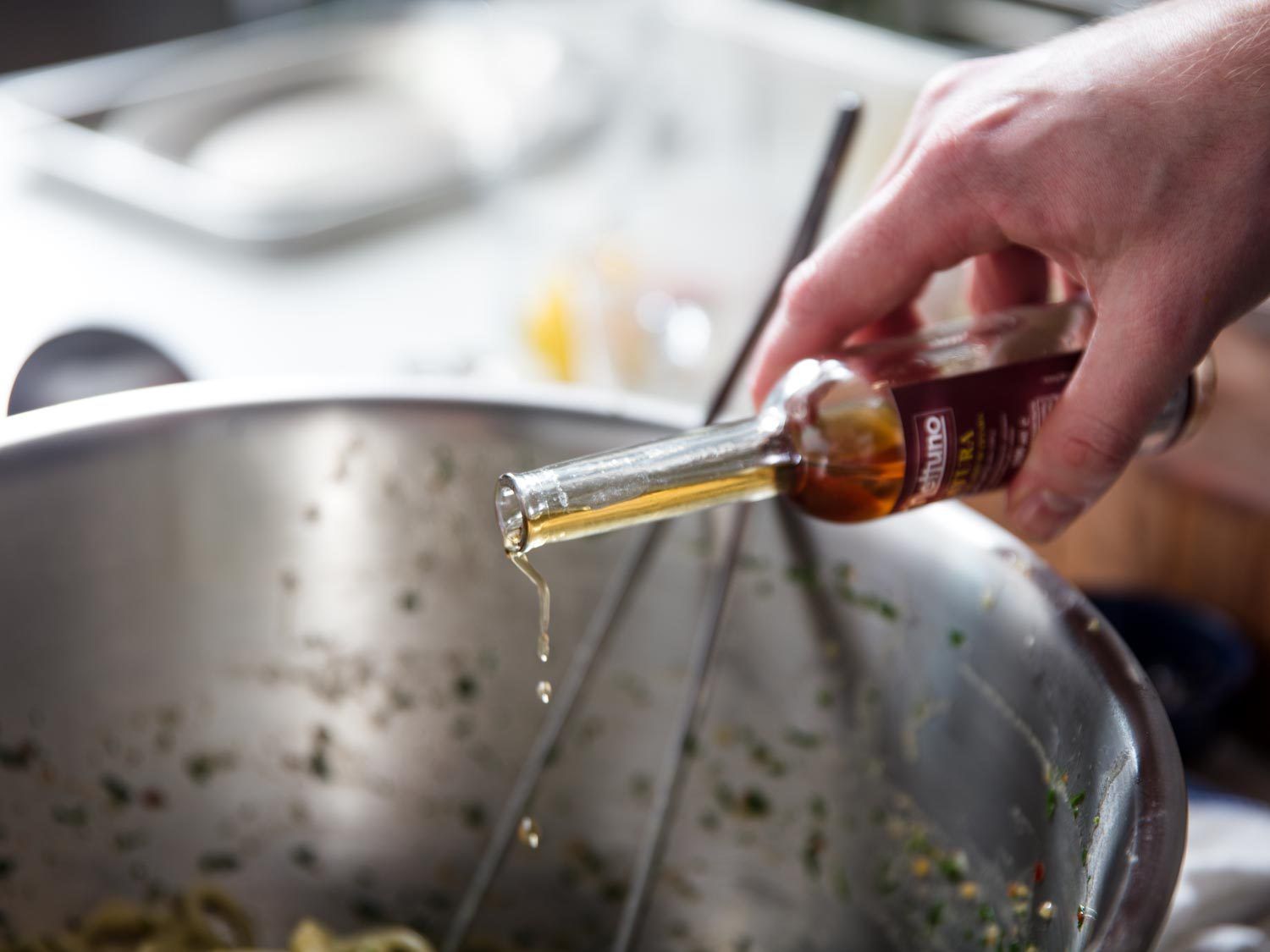 Drizzling colatura into a mixing bowl of pasta con la colatura di alici.