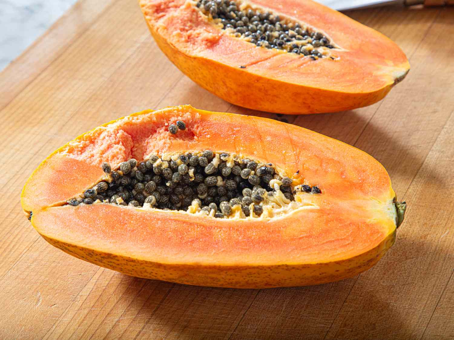Two halved papayas with visible seeds on a wooden surface