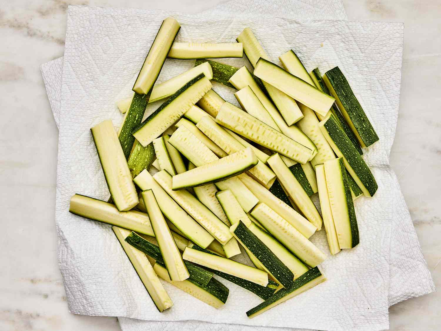 Long sliced zucchinis on paper towels on a marble tabletop 