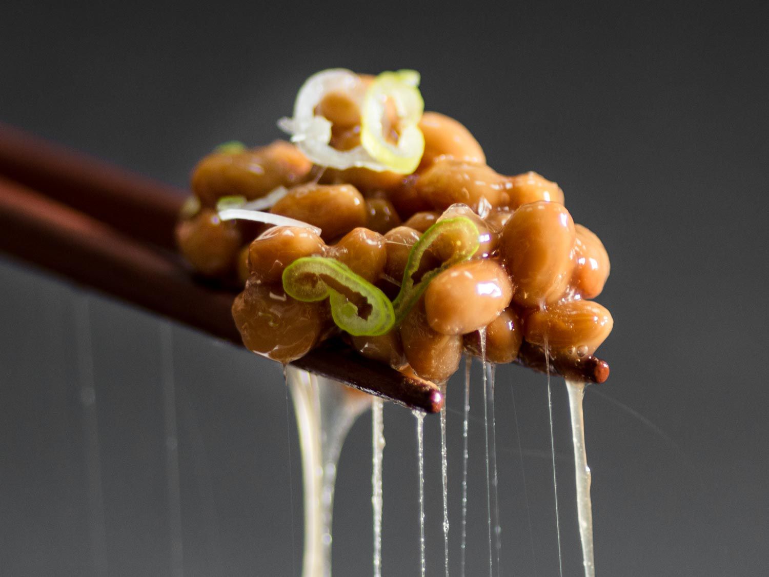 Closeup of chopsticks holding a bite of scallion-flecked natto.