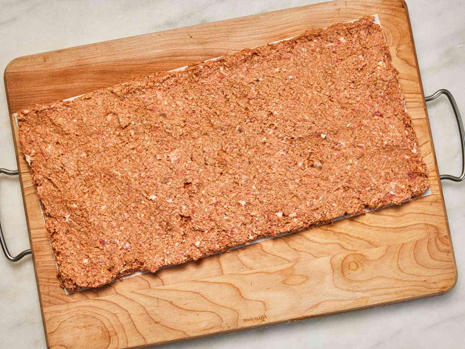 Overhead view of meat mixture spread into thin layer on parchment paper to form a rectangle.
