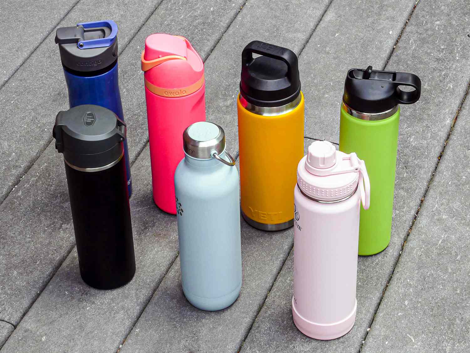 Seven stainless steel water bottles on a grey surface