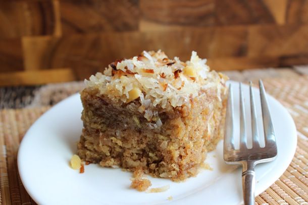Slice of oatmeal cake with a topping of coconut and nuts on a white plate with a fork on a wooden background