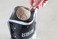 A hand scooping powdered substance from an open pouch labeled 'Everyday Dose' with a spoon
