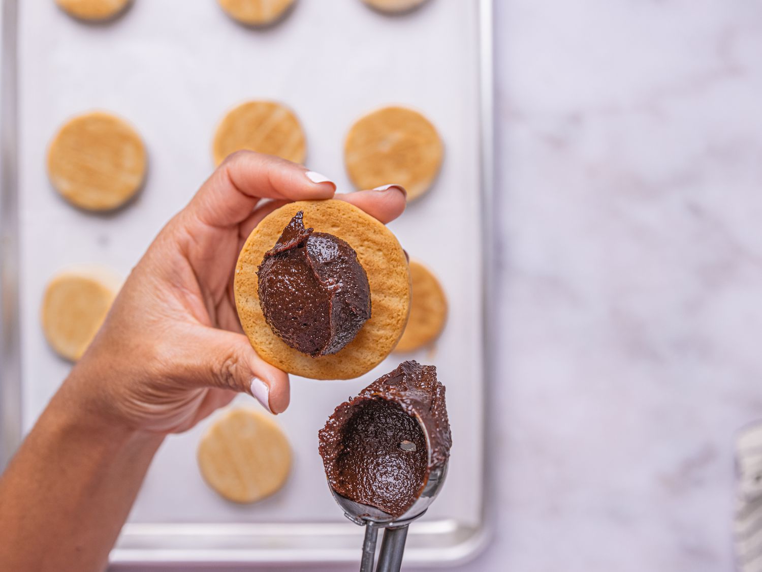 Spooning fudge onto cookies, cookies on sheetpan in background 