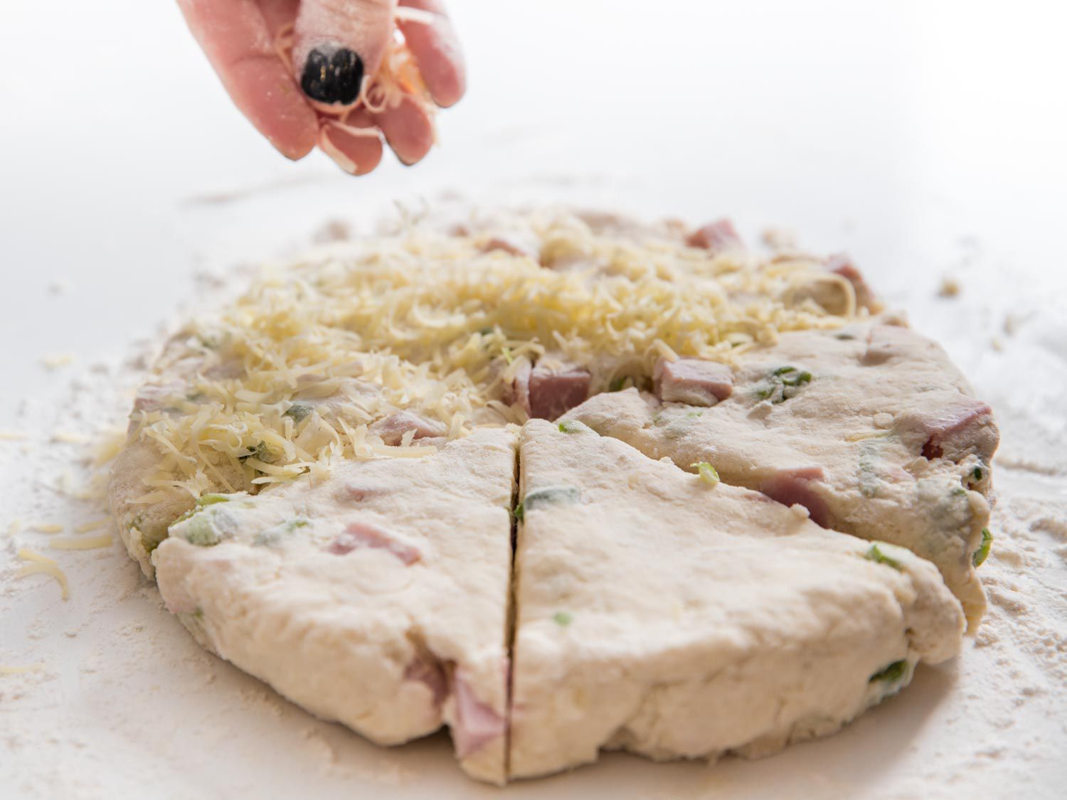 Cutting scone dough into wedges and sprinkling with cheese.