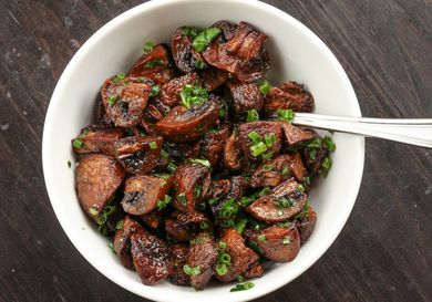 Roasted quartered cremini mushrooms tossed with chopped chives in a white bowl.