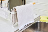 A tan kitchen towel hanging off of a dish rack.