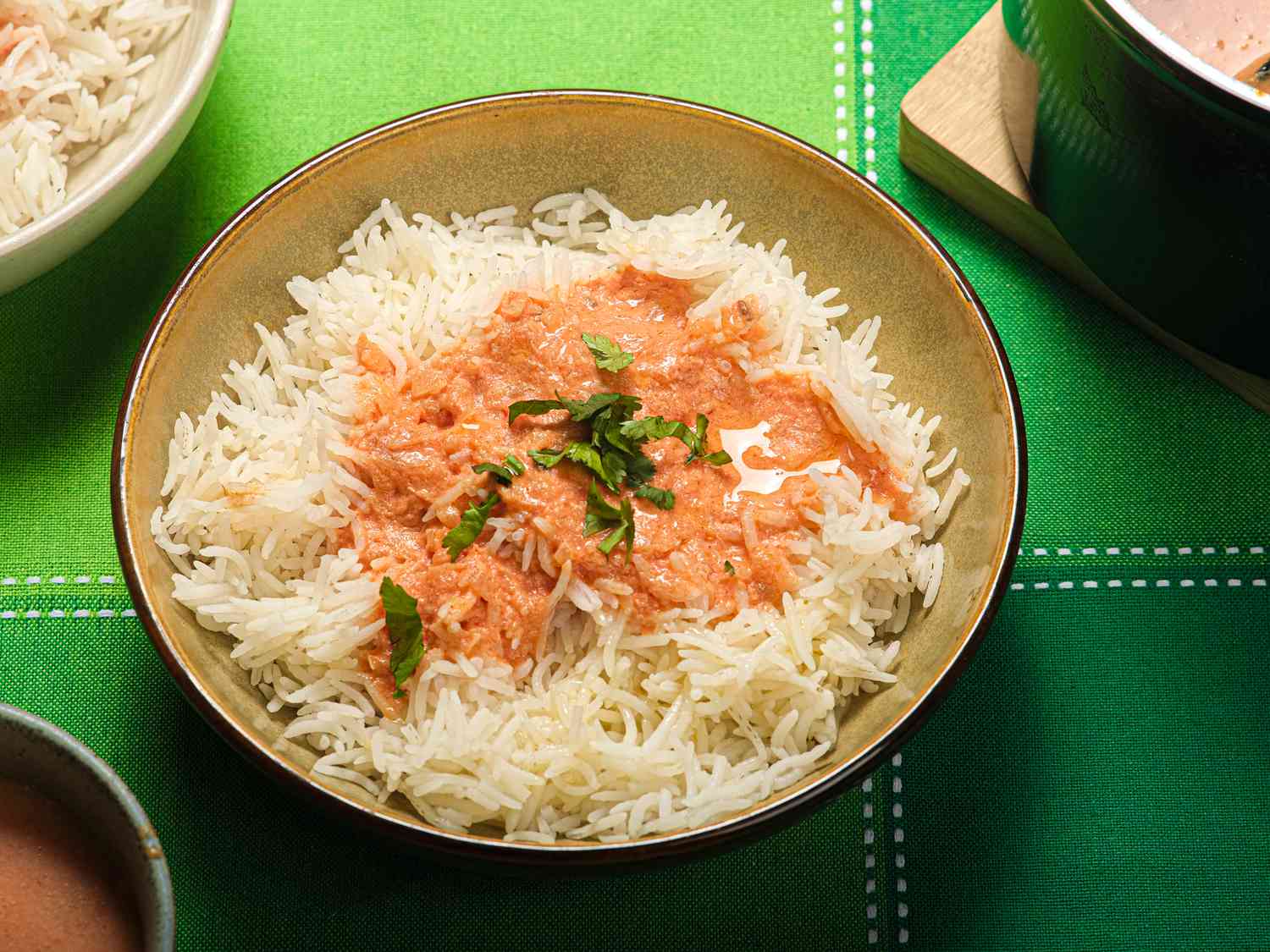 Bowls of rice and Tomato Coconut soup, dutch oven on the side, and green tabletop.