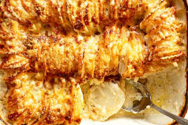 Browned hasselback potatoes being served with a spoon.