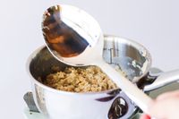 A closeup of oatmeal being stirred in a metal pot with a large metal spoon