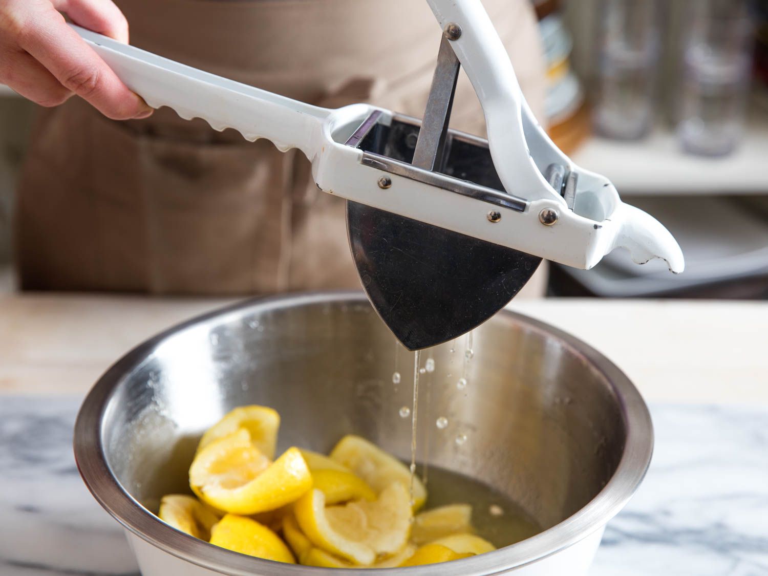 Using a potato ricer to squeeze juice and sugar syrup from lemon rinds.