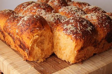 Closeup of pizza bread being cut into rolls on a bamboo cutting board.