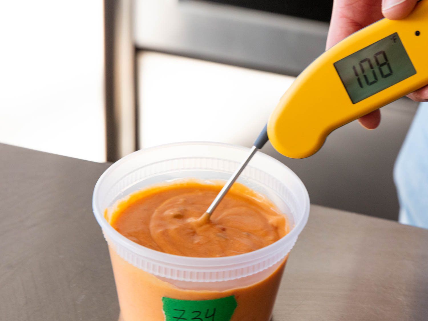 Using a thermometer to measure the temperature of queso dip in a plastic container.