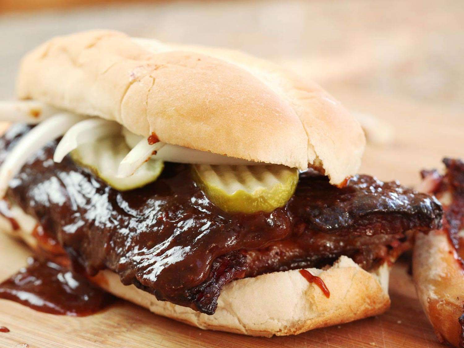 A homemade rib sandwich on a bun, topped with pickles and onions.
