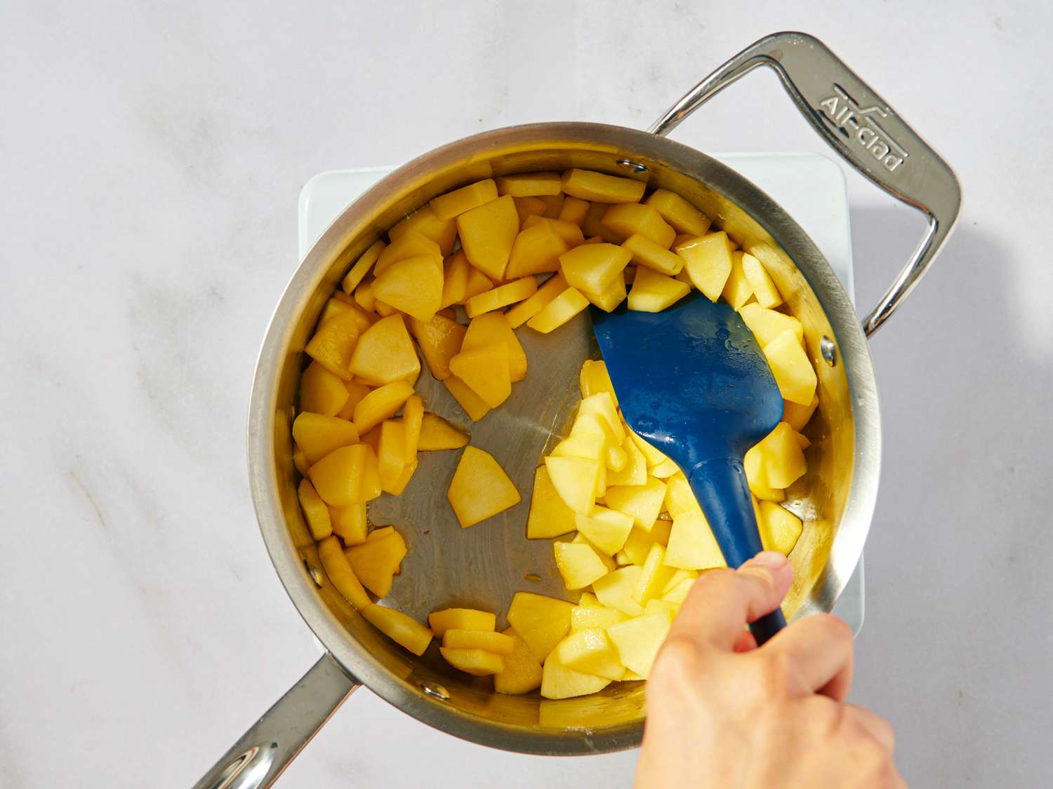 Cooking diced apples in a saucepan with a blue spatula