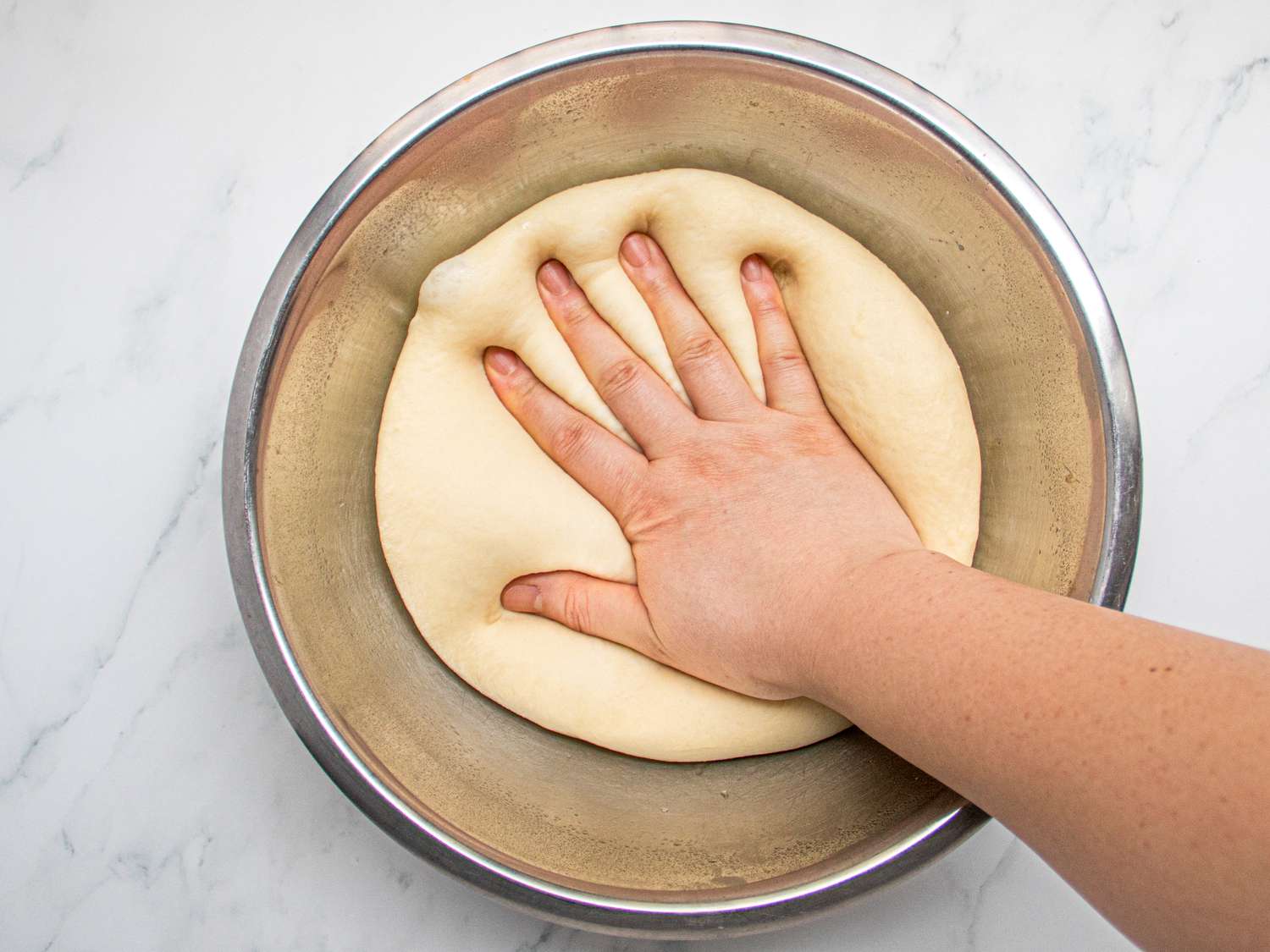 Overhead view of punching down dough in bowl
