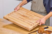Person holding a John Boos Reversible Maple Wood Cutting Board with Juice Groove over a table with food and a knife