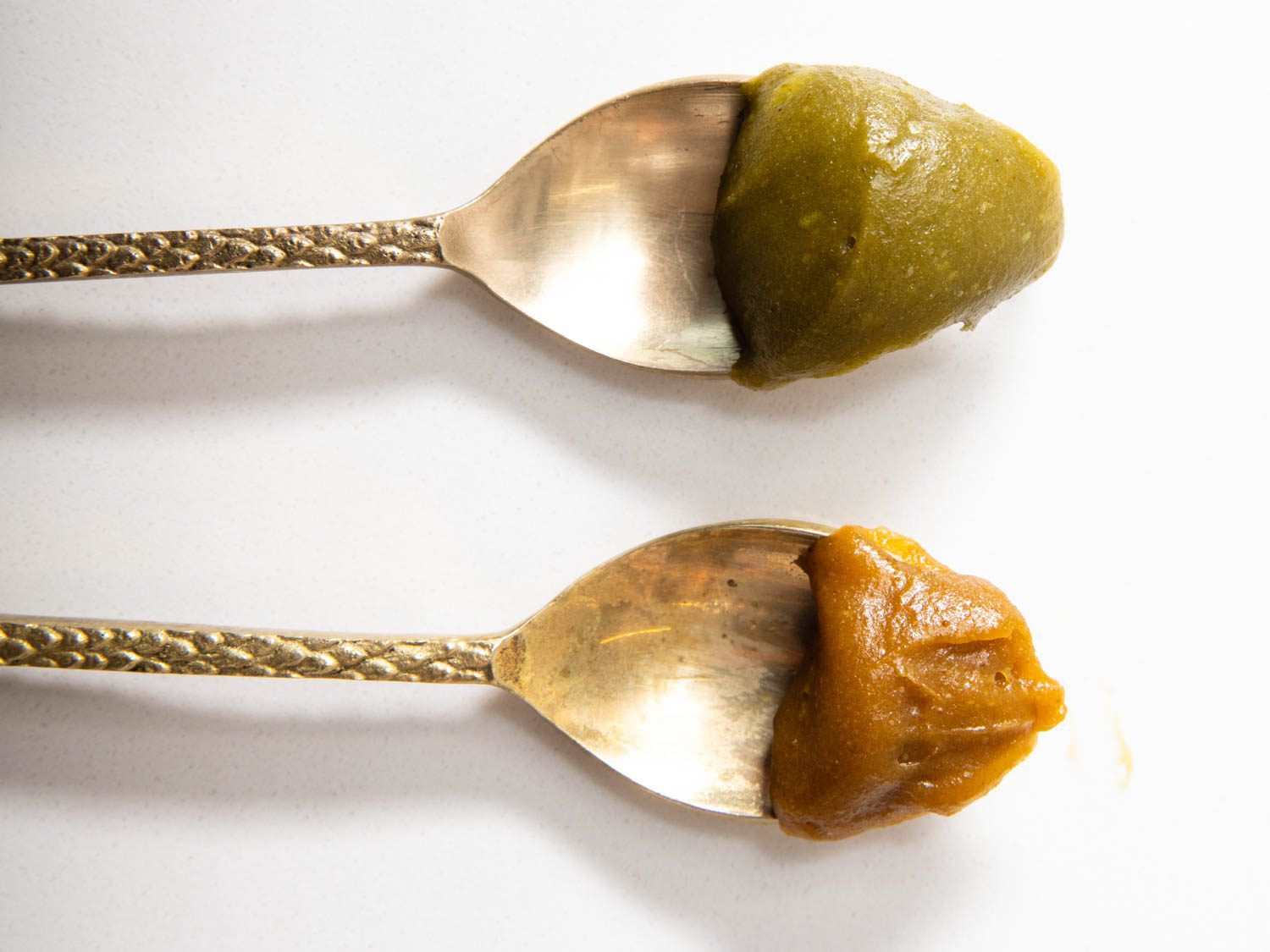 A spoon of toasted pistachio paste, with food coloring on top (green color) and without food coloring on bottom (brown).