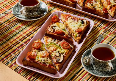 Slices of pizza toast arranged on a tray with cups of tea